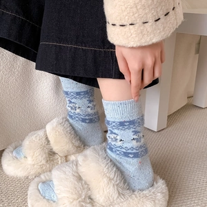Detailansicht hellblauer Wollsocken mit Rentiermuster und weißen flauschigen Hausschuhen