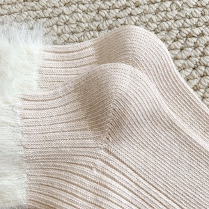 Close-up of pink cable-knit thermal socks with plush white faux fur trim on cozy carpet