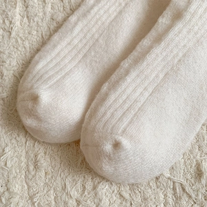 Gros plan de chaussettes en laine crème montrant la texture côtelée et la matière douce
