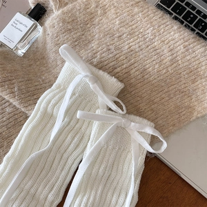 Detailed close-up of white ribbed knit leg warmers with elegant silk bow accents