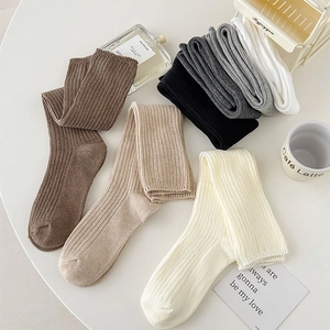 Neutral colored ribbed knit calf socks displayed on a table in a minimalist aesthetic