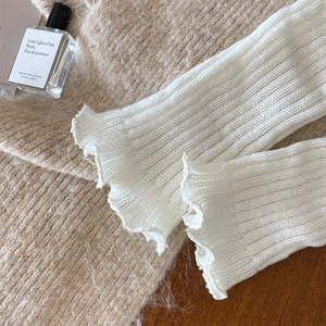Macro detail of white ribbed knit leg warmers with delicate ruffle edges on wood background