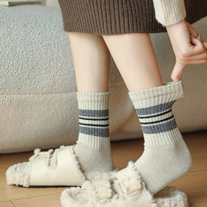 Detail of wool knit socks with gray stripes and warm fleece-lined slippers on wood floor