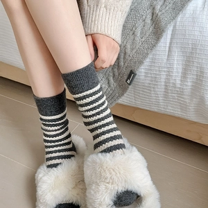 Close-up of thick knitted grey and white striped wool socks worn with plush slippers