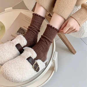 Close-up of cozy cream wool socks with ruffle cuffs paired with fuzzy sherpa mules