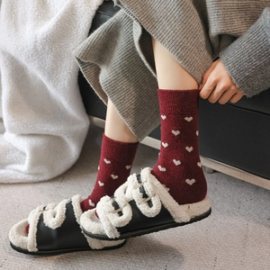Close-up of burgundy wool socks with white heart patterns and fuzzy slippers