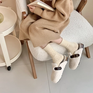 Close-up of cream faux shearling mule slippers with brown buckle strap and warm socks