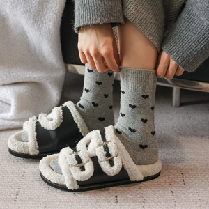 Detail of black buckled slides with white faux fur lining and grey heart knit socks