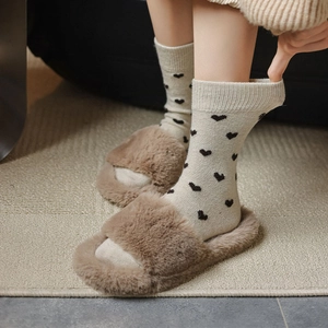 Detail of beige knitted crew socks with black heart patterns and faux fur slippers