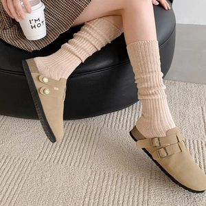 Close-up of suede buckle mules paired with chunky knit slouch socks in a cozy setting
