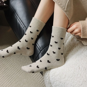 Close-up of beige knitted wool socks with black heart pattern and ribbed cuff detail