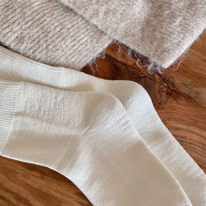 Close-up of cream-white knitted crew socks with fine texture on a warm wooden surface