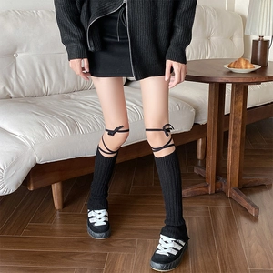 Close-up of black knitted leg warmers with ribbon bow ties and vertical stripe texture