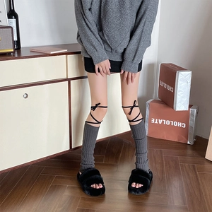 Close-up of gray ribbed knit leg warmers with black ribbon bows and platform plush slippers