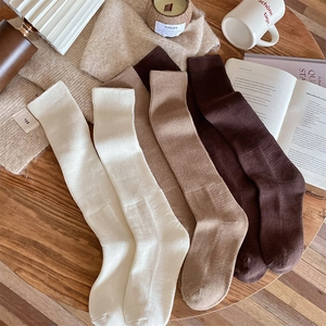 Close-up of knit calf socks in earth tones on a wooden table with cozy autumn props