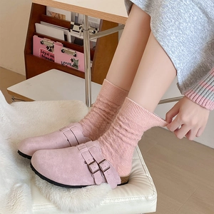 Close-up of pink suede mule shoes with buckles and textured wool socks on white fur
