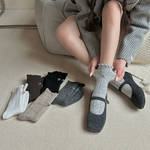 Detail of wool socks featuring ruffled cuffs and delicate black bow embroidery detail