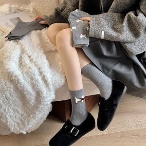 Detailed knit of grey mid-calf socks with white puppy motif and red ribbon bow