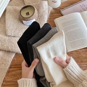 Close-up of four-color knit calf socks in black, grey, and cream on a cozy winter table