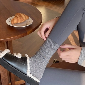 Close-up of grey ribbed knit socks paired with black plush slippers in a home setting