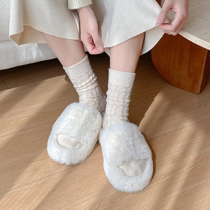 White faux fur slippers with quilted socks on wooden floor in warm sunlight