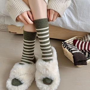 Detail of green and white striped wool socks paired with white fuzzy slippers in a cozy room