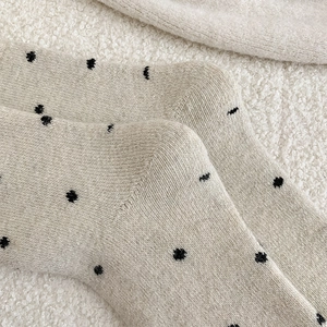 Close-up of oatmeal wool socks with black polka dots on white fleece background