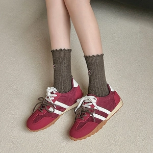 Close-up of olive green wool socks with pink bow embroidery and burgundy suede sneakers