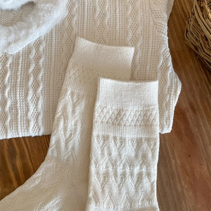 Detail of cream cable-knit socks and sweater with faux fur collar on wooden surface