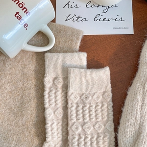 Close-up of beige knit socks with textured diamond and polka dot patterns on wood