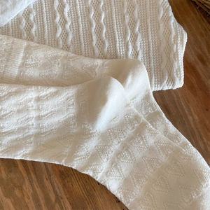 Macro shot of creamy white knitted socks with delicate hollowed heart pattern on wood