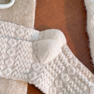Close-up of cream knit wool socks showing embossed wave and diamond geometric patterns