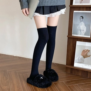 Detail of black knitted over-knee socks paired with plush faux fur slippers at home