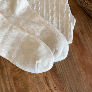 Macro detail of white knitted socks featuring diamond lattice and cable stitch texture
