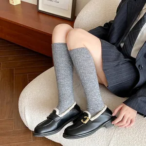 Women's cashmere knee-high socks with black loafers and gold buckle in a cozy home setting