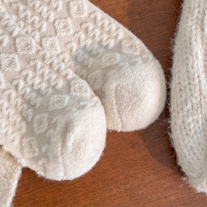 Detailed macro view of cream wool socks featuring relief wave patterns and chunky knit texture