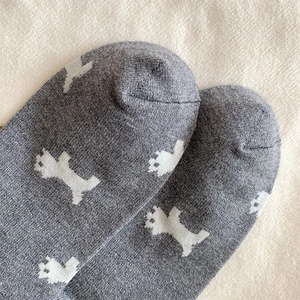 Detail of gray knitted socks featuring white terrier puppy patterns and seamless toe design
