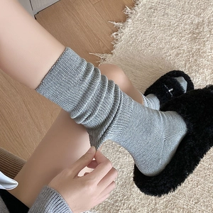 Detail of grey knitted slouch socks with ribbed texture paired with black faux fur slippers