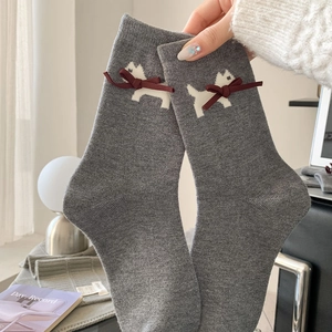 Detail of grey knitted socks featuring a white dog pattern and a red ribbon bow decoration