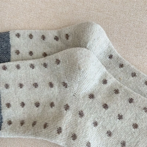 Détail de chaussettes en laine tricotée beige à pois marron et talon gris chiné