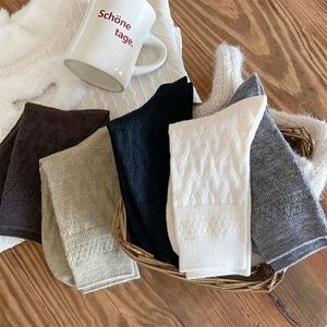 Detail of wool blend socks in five colors with textured knit patterns in a rustic basket
