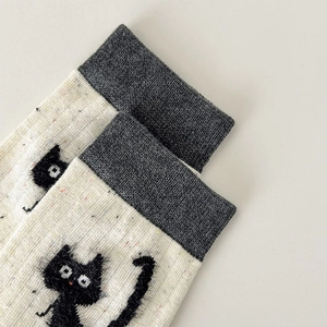 Macro detail of knit mid-calf socks with colorful flecks and 3D plush cat embroidery
