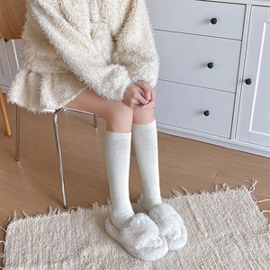 Close-up of white ribbed knit socks and plush slippers on warm wooden flooring