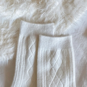 Detail of white cashmere knit socks with diamond texture on soft plush background