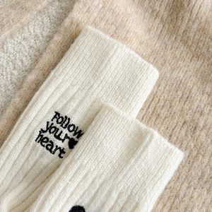 Detailed close-up of 'Follow your heart' letter embroidery on white ribbed knit socks