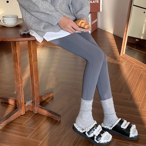 Detail of dark grey ribbed socks and leggings paired with black plush slippers on wood