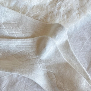 Detail of cream argyle cashmere socks featuring ribbed cuffs on a plush background
