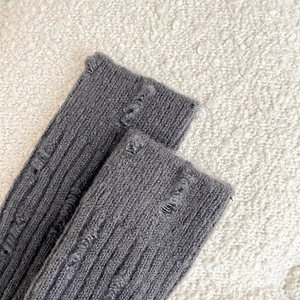 Detailed close-up of grey ribbed knit leg warmer with stylish distressed ripped holes