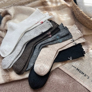 Detail of wool socks featuring ruffled cuffs and delicate embroidered bow accents
