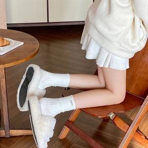 Close-up of white plush slippers with thick black non-slip soles in a cozy home setting